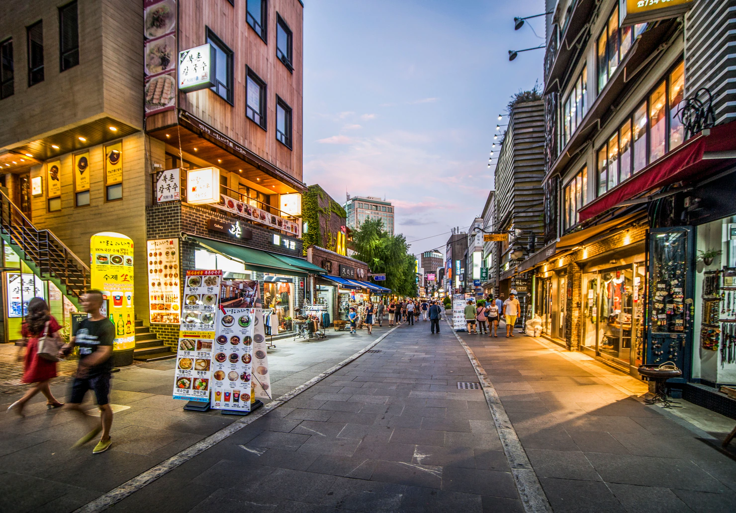 Peatones caminando frente a tiendas y restaurantes iluminados en una calle de Insadong al anochecer.