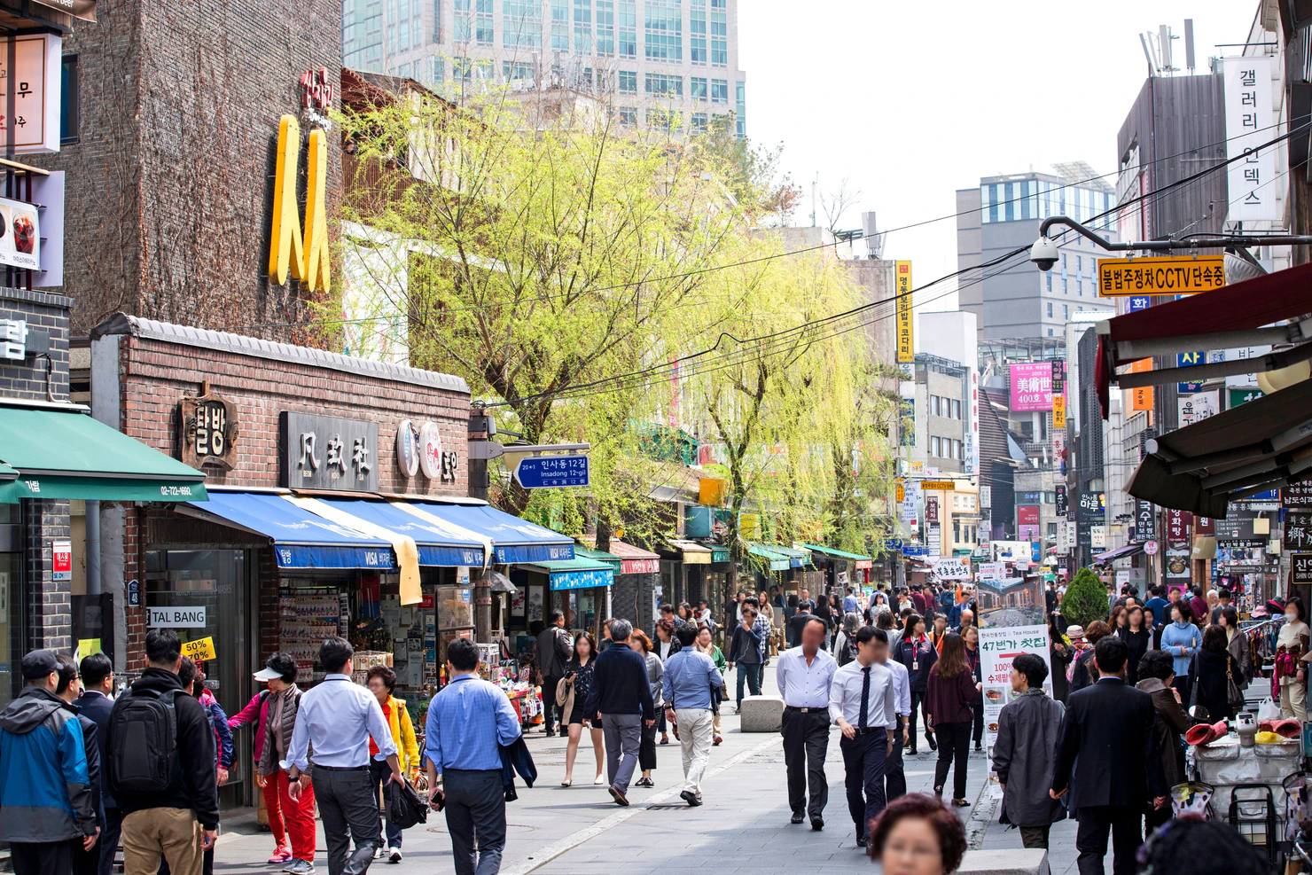 Multitud caminando por Insadong-gil entre tiendas, galerías y árboles en Seúl.