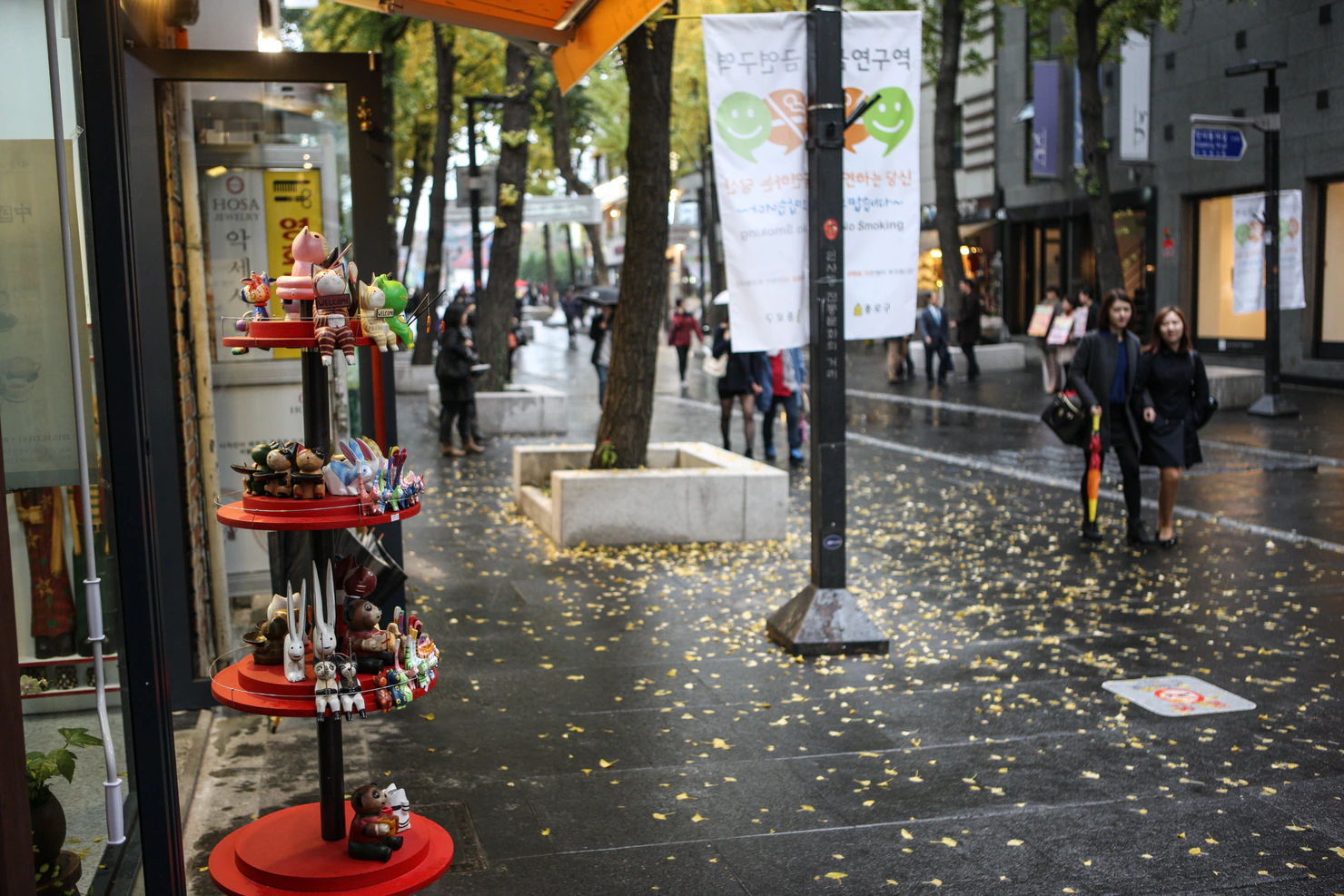 Pequeñas figuras decorativas fuera de una tienda junto a un paseo mojado y cubierto de hojas en Insadong.