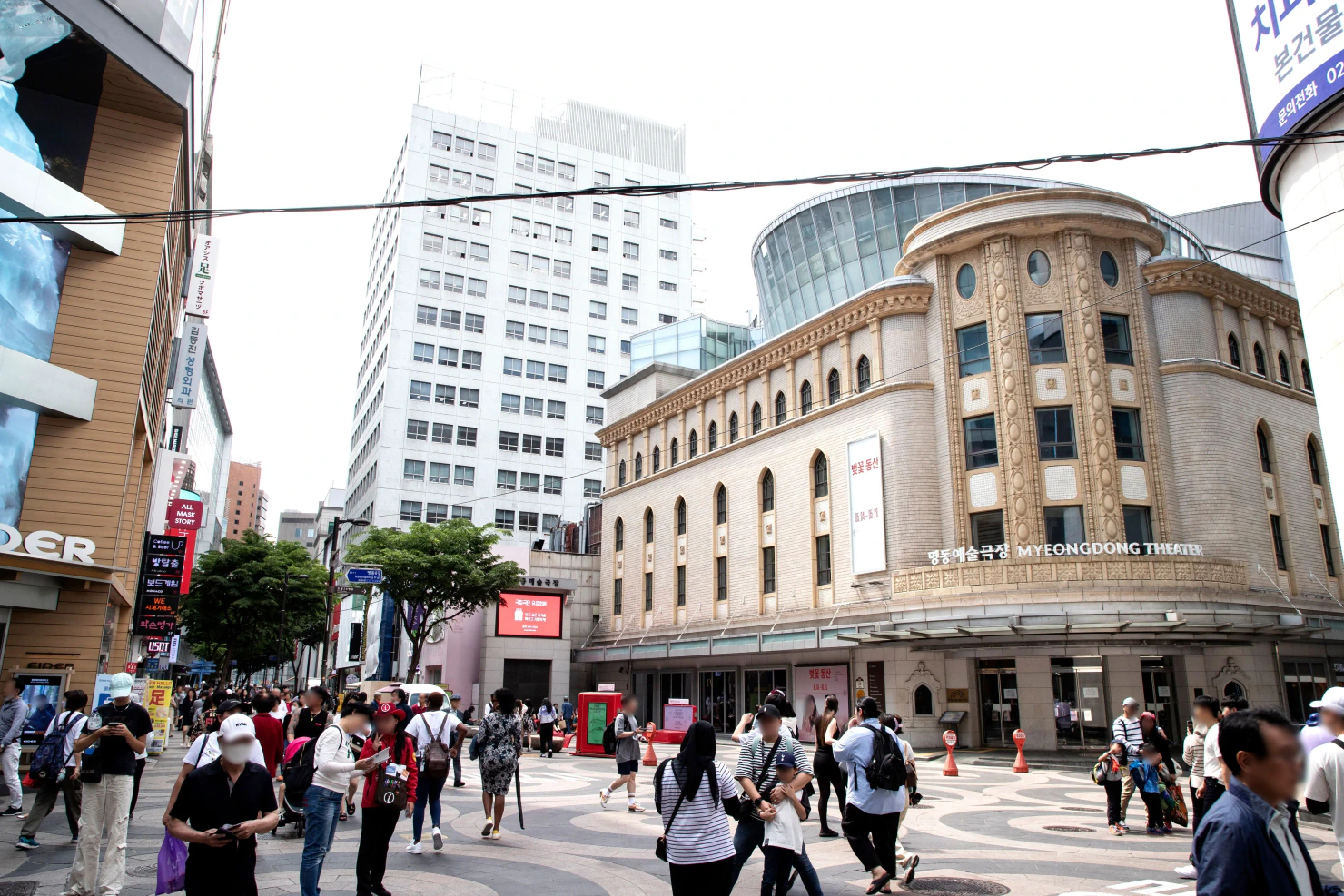 Pedestrians walking past Myeongdong Theater and nearby shops in Seoul.